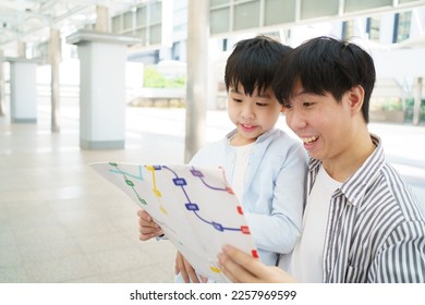 Happy cheerful Asian family traveling in the downtown together concept. Father looking at the railway station map with his son and pointing a forefinger on the map. Asian family tourist in city. - Shutterstock ID 2257969599