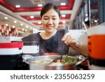 Happy - cheerful Asian fat woman enjoy eating a traditional Asian Hotpot or Sukiyaki in the Asian Hotpot restaurant. Woman using chopsticks pickup a pork belly and drip into boiled soup.