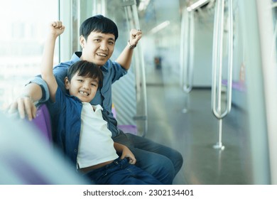 Happy cheerful Asian father and son traveling in the city on the sky train, man taking his lovely son travel on the city sky train.