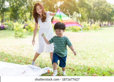 Happy Cheerful Asian Little Boy Running And Playing With Kite Flying With Mother Outdoor In The Park. Little Boy And Mother Having Fun, Enjoy, Relaxing With Kite Flying Together. Family, Kid, Playing 