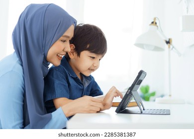 Happy cheerful Asian muslim woman woman teaching her little son a drawing on digital tablet, mother let her little young boy doing a school homework or an online learning on tablet. - Powered by Shutterstock