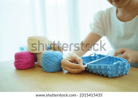 Happy cheerful Asian woman doing a crochet in living room in free time. Skillful Asian craftswoman knitting a handcraft crochet and using measurement tape to measure size of work piece.