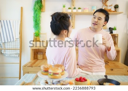 Happy cheerful Asian young couple in kitchen in morning, couple drinking a hot coffee and talking together in kitchen. Lovely young couple or husband and wife relaxing in morning and drinking coffee.