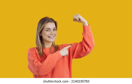 Happy Cheerful Assertive Active Energetic Independent Pretty Blonde Caucasian Woman Smiling, Looking At Camera, Flexing And Pointing At Her Arm Demonstrating Strong Bicep Muscle. Girl Power Concept