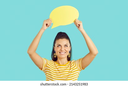 Happy Cheerful Beautiful Young Woman Standing Isolated On Bright Turquoise Color Background, Smiling And Holding Clean Blank Yellow Paper Mock Up Speech Balloon, Thinking Cloud Or Word Bubble