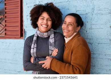 Happy cheerful black adult daughter and mother with broad smile embracing each other outside humble home Togetherness, family, support concept.