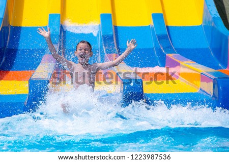 Happy cheerful boy splashing water on water slide at aqua park