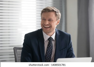 Happy Cheerful Business Man Ceo In Suit Laughing Sit At Work Desk With Laptop, Smiling Male Executive Looking Away Having Fun At Workplace Feel Joy Enjoying Funny Positive Moments In Corporate Office