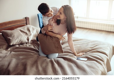 Happy Cheerful Caucasian Mother And Little Teen Son Hugging And Playing In Bedroom.