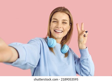 Happy cheerful confident young online social media blogger girl takes selfie photo on pink color background. Positive high school student holding mobile phone, smiling and doing peace victory - Powered by Shutterstock