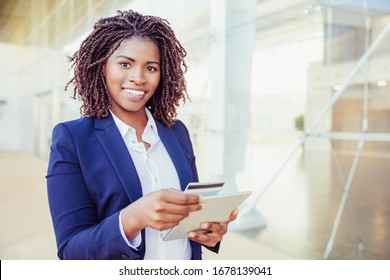Happy Cheerful Customer Paying Online. Young African American Business Woman Standing Outside, Using Tablet, Holding Credit Card. Mobile Banking Concept