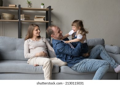 Happy Cheerful Dad Tickling Playful Excited Little Daughter Girl, Playing Active Games With Kid At Home, Cuddling Child With Love, Tenderness, Enjoying Parenthood. Pregnant Mom Smiling, Laughing