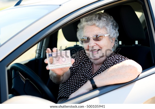happy cheerful elderly senior woman\
driving her car and showing her drivers\
license