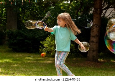 Happy cheerful elementary school age child, girl playing with soap bubbles alone outdoors, summer, one person bubble popping Happiness, having fun, childhood energy, movement concept, people lifestyle