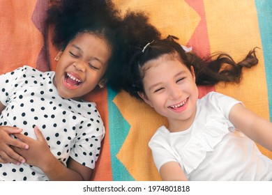 Happy Cheerful Ethnic Girls  Laying On Mat At Outdoors Park, Her Smiling And Laughing Together, Relationship Little Kids, Diverse Ethnic Concept.