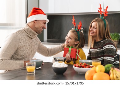 Happy Cheerful Family Exchanging With Christmas Presents While Having Breakfast At The Kitchen