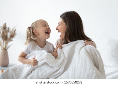 Happy Cheerful Family Young Adult Mother Having Fun Playing With Adorable Cute Little Kid Child Daughter Holding Warm White Duvet Laughing Relaxing In Cozy Bed In Morning Enjoying Family Lifestyle