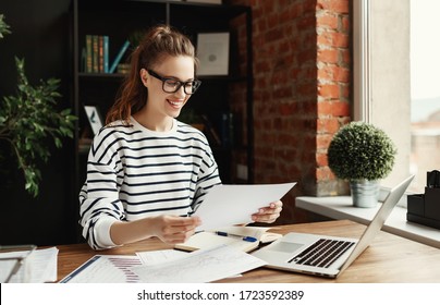 Happy cheerful female freelancer in glasses and casual clothes analyzing information in documents while sitting at table with graphics and notepad and using laptop in cozy contemporary apartment  
 - Powered by Shutterstock