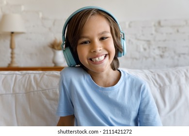 Happy cheerful gen Z school kid boy in big headphones looking at camera with toothy smile, talking on video conference call, studying online from home, attending virtual lesson. Head shot portrait