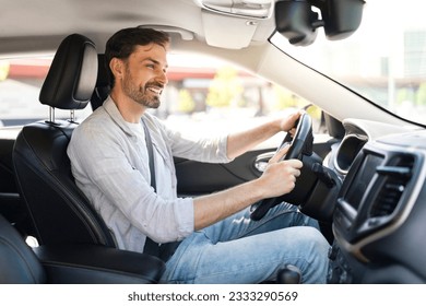 Happy cheerful handsome bearded young man wearing casual outfit driver sitting in front seat, holding auto steering wheel, driving his brand new nice car and smiling, copy space - Powered by Shutterstock