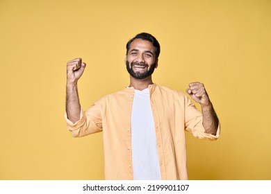 Happy Cheerful Indian Man Winner Winning Face Expression Raising Fists In Yes Gesture Screaming About Lottery Betting Money Win Celebrating Great Prize, Got Job Offer Isolated On Yellow Background.