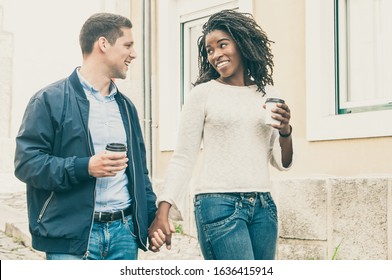Happy cheerful interracial couple enjoying date. Afro American girl and her Caucasian boyfriend holding hands, walking around old city and enjoying coffee break. Love and leisure concept