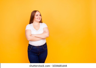 Happy Cheerful Joyful Confident With Chubby Face Oversize Woman Wearing Casual Tshirt And Dark Blue Jeans, Standing With Folded Arms, Looking At Empty Blank Space Isolated On Bright Yellow Background