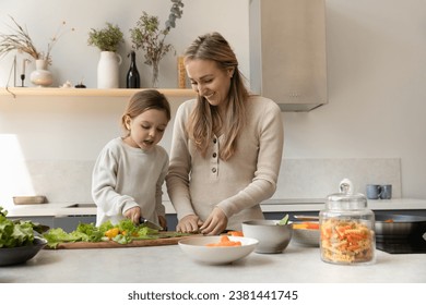 Happy cheerful mother teaching sweet daughter girl to cook healthy dinner. Mom and kid cutting fresh vegetables for salad, preparing organic ingredients in kitchen. Family eating concept - Powered by Shutterstock