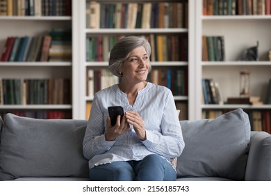 Happy Cheerful Older Grey Haired Woman Holding Cellphone, Using Online Application On Smartphone, Looking At Window Away, Thinking Over Shopping On Internet, Order, Purchase, Texting Message