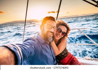 Happy and cheerful people enjoying the travel and trip on a sail boat with ocean and sunset sunlight in background - traveler lifestyle for adult man and woman smiling doing a selfie picture