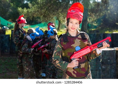 Happy Cheerful Positive Teen Girl Wearing Uniform And Holding Gun Ready For Playing With Friends On Paintball Outdoor