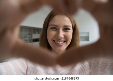 Happy Cheerful Pretty Adult Woman Looking At Camera Through Finger Heart Shaped Frame, Joining Hands, Smiling Posing Indoors. Joyful Blogger Girl Showing Love, Support, Gratitude Symbol. Close Up