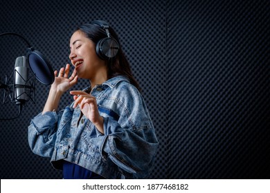 Happy cheerful pretty smiling of portrait of young Asian woman vocalist Wearing Headphones recording a song front of microphone in a professional studio - Powered by Shutterstock