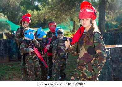 Happy Cheerful Smiling Teen Girl Wearing Uniform And Holding Gun Ready For Playing With Friends On Paintball Outdoor