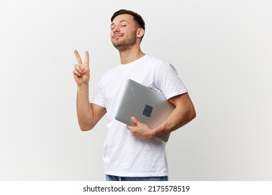 Happy cheerful tanned handsome man in basic t-shirt show v sign gesture hold laptop pc posing isolated on over white studio background. Copy space Banner Mockup. Electronics repair concept