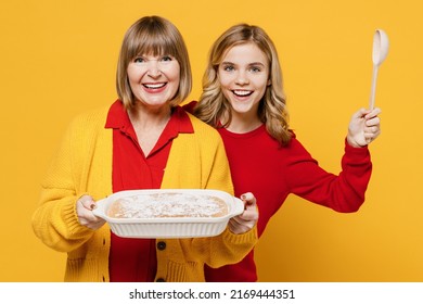 Happy Cheerful Woman 50s In Red Shirt Have Fun With Teenager Girl 12-13 Years Old Grandmother Granddaughter Hold Spoon Meal Dish Casserole Isolated On Plain Yellow Background Family Lifestyle Concept