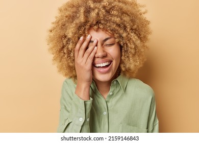 Happy cheerful woman makes face palm laughs joyfully expresses sincere feelings and positive emotions dressed in casual linen shirt isolated over brown background. Peope and happiness concept