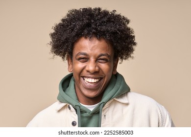 Стоковая фотография: Happy cheerful young African American gen z guy isolated on beige background. Smiling funny ethnic teen student, cool curly generation z teenager laughing with white perfect teeth, close up portrait.