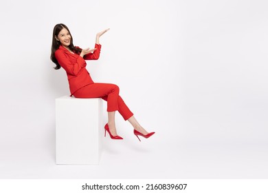 Happy cheerful young Asian businesswoman in red suit sitting on white box isolated on white background, Presentation concept - Shutterstock ID 2160839607