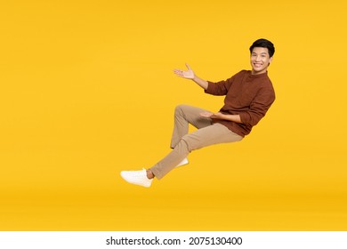 Happy cheerful young Asian man floating in the air isolated on yellow background, Presentation concept