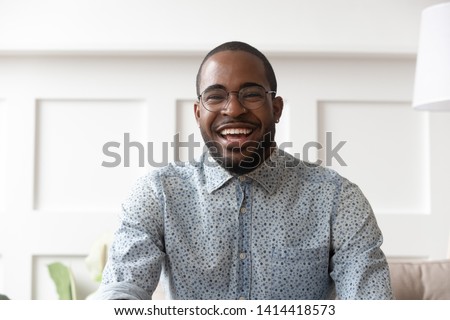 Happy cheerful young black man video calling looking at camera at home, smiling african guy communicate in internet chat recording vlog talking laughing enjoy online conversation, webcam view