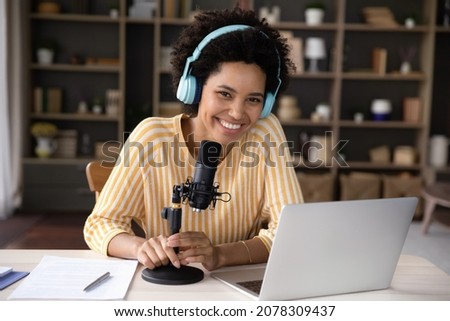 Happy cheerful young Black woman in headphones and professional microphone recording audio podcast for radio, live channel on internet, presenting news on air. Newscaster, blogger head shot portrait