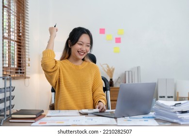 Happy Cheerful Young Female Sitting At Desk With Calculator And Laptop Holding Pen Having Overjoyed Look, Exclaiming Yes With Excitement, Finally Paid Off Mortgage Debt, Feeling Free