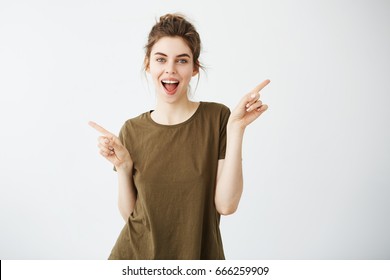 Happy Cheerful Young Girl Looking At Camera Smiling With Opened Mouth Pointing Fingers In Side Over White Background.