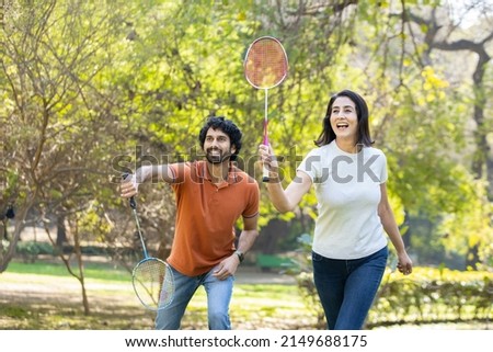 Happy cheerful young indian couple playing badminton game together in the park. urban asian sporty man and woman having fun outdoor sports and game activity concept. picnic and vacation.