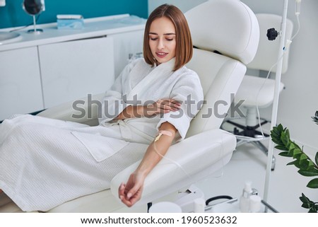 Happy cheerful young lady resting at the intravenous vitamin drip treatment in spa salon