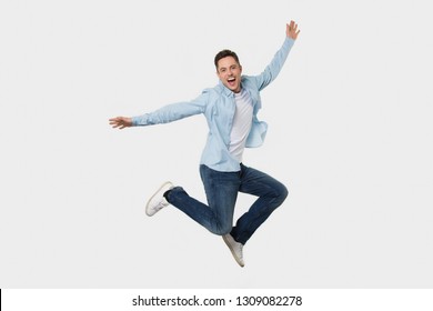 Happy Cheerful Young Man Jumping Feeling Joy, Excited Funny Energetic Guy Winner Fly Rejoicing Success Looking At Camera Screaming Isolated On White Grey Studio Background, Full Body Length Portrait