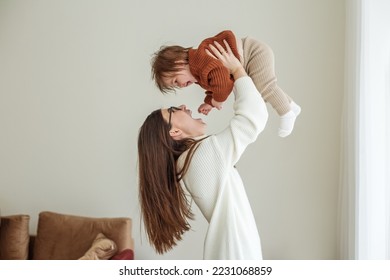 Happy cheerful young mother throws an adorable baby in air, plays, hugs baby with love, care, enjoys motherhood, maternity leave. Family spends time together. - Shutterstock ID 2231068859