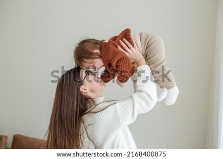 Happy cheerful young mother throws an adorable baby in air, plays, hugs baby with love, care, enjoys motherhood, maternity leave. Family spends time together.