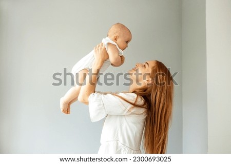 Happy cheerful young mother throws an adorable baby in air, plays, hugs baby with love, care, enjoys motherhood, maternity leave. Family spends time together.